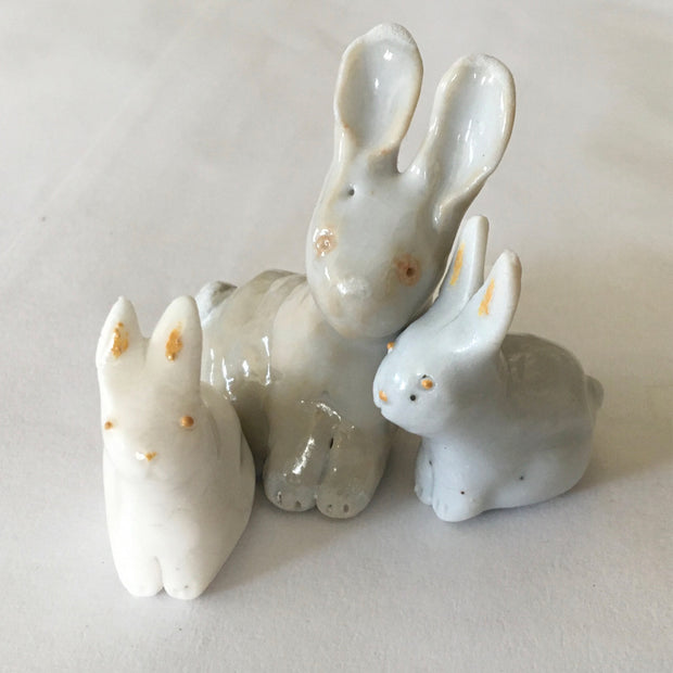 3 porcelain bunnies, one slightly larger and 2 smaller ones cuddled into each other. They have golden eyes, noses and the babies have golden ear colorings.