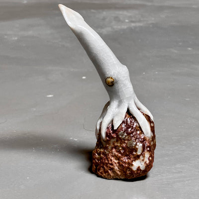Ceramic sculpture of a long headed squid atop of a cratered moon, with rusted red coloring.