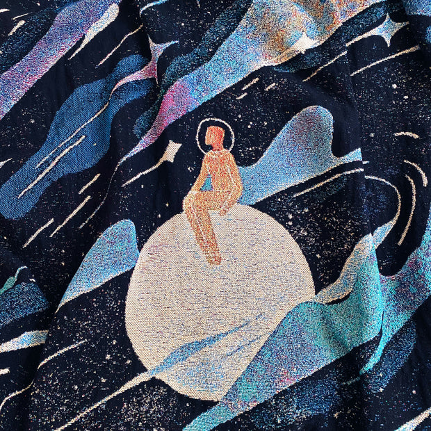  Close up of tapestry with a figure in an orange space suit and helmet, sitting on a moon.