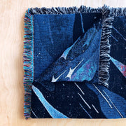 Close up photo of folded tapestry blanket, showing the intentional side fraying and blue space pattern design.
