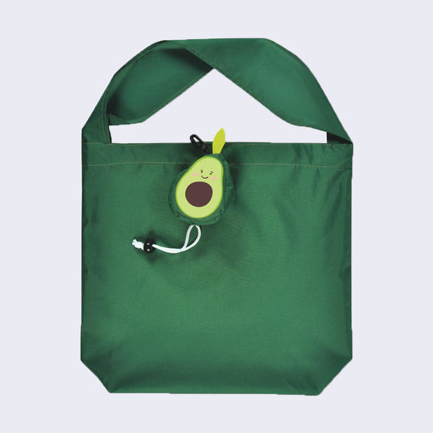 A green polyester tote with a short, thick handle and a small smiling avocado attached by a white drawstring.