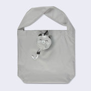 A gray polyester tote bag with a short, thick handle. Clipped to the top center of the bag is a round, smiling gray cat face with white accents.