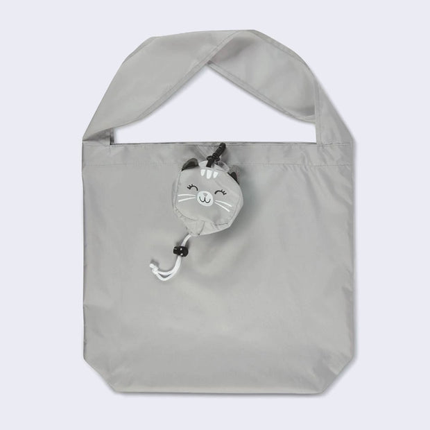A gray polyester tote bag with a short, thick handle. Clipped to the top center of the bag is a round, smiling gray cat face with white accents.