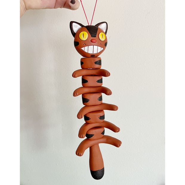 Sculpture of a pieced together Catbus, stacked atop itself like a spine. It hangs from a red string.
