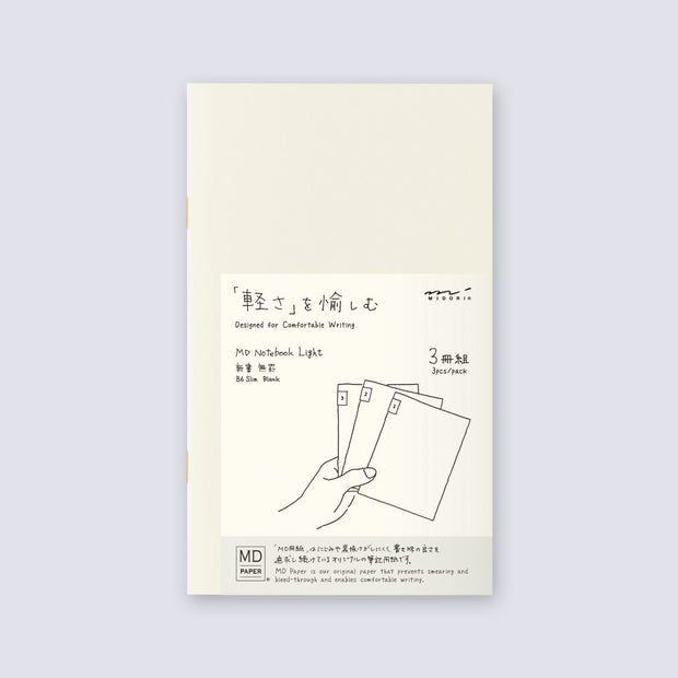 Cream colored blank cover journal within packaging with a cream color insert that has Japanese writing and an illustration of a hand holding 3 notebooks.