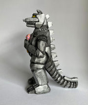 Side view of a carved wooden sculpture of a mechanized Godzilla, painted silver and black with bright yellow eyes, holding a strawberry ice cream cone with sprinkles.