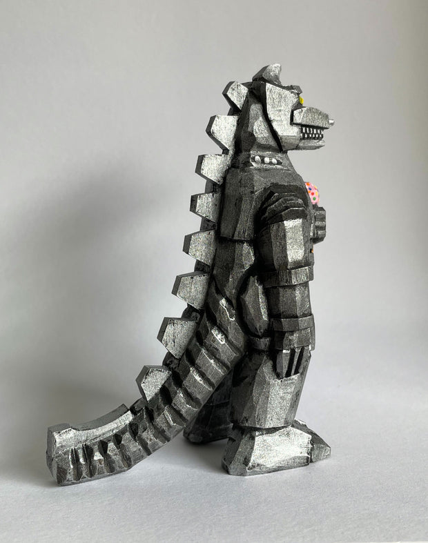 Side view of a carved wooden sculpture of a mechanized Godzilla, painted silver and black with lots of back spikes and a long tail.