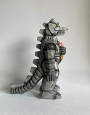 Side view of a carved wooden sculpture of a mechanized Godzilla, painted silver and black with bright yellow eyes, holding a strawberry ice cream cone with sprinkles.