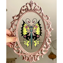 Small painting of a tattoo style yellow, pink and black butterfly on a clear acrylic sheet in a very ornate pink frame.