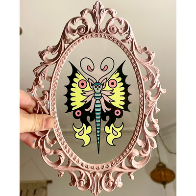 Small painting of a tattoo style yellow, pink and black butterfly on a clear acrylic sheet in a very ornate pink frame.