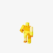 Wooden robot made of square-like shapes, standing with an arm on its hip. It is various shades of yellow.