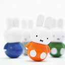 A plastic Miffy figure wearing an orange shirt with a rounded bottom, wobbling slightly on a tilt. More wobble Miffy figures are out of focus in the background.