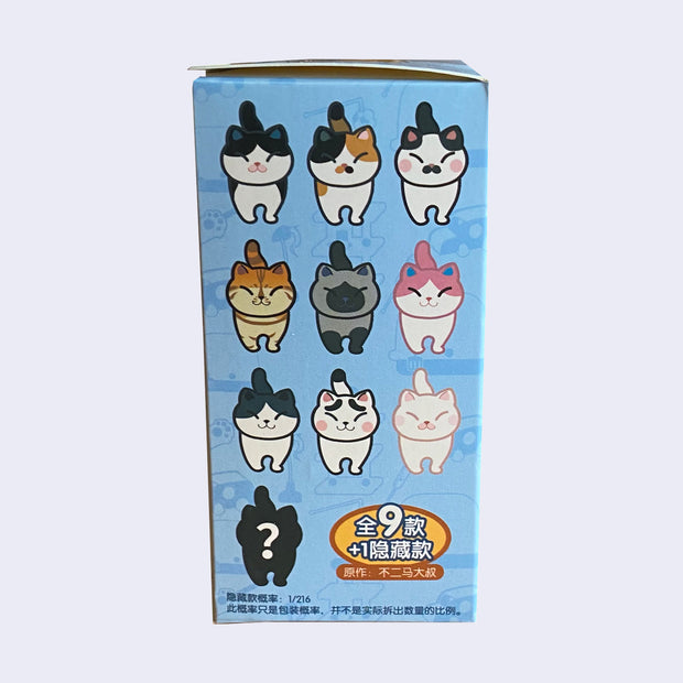 Side of display box, showing 9 chubby cat blind box options: white with black, calico, white with black and pink cheeks, orange tabby, Siamese, white with pink, white with gray, white with black eyebrows, and all white. 