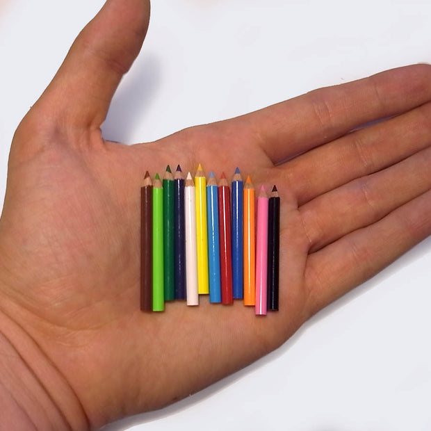 Set of 12 very miniature, yet functional colored pencils, all sharpened and being held side by side in the palm of someone's hand.