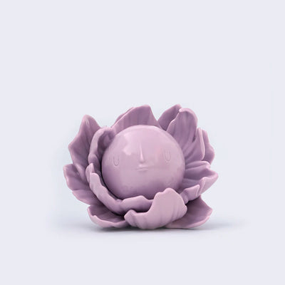 Lavender colored vinyl figure of a round full moon with a small minimalistic face. It sits within a series of flower petals, as if it is the pistil of the flower.