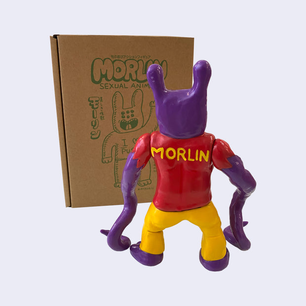 Back view of purple painted soft vinyl figure, with two bunny like ears. The figure is muscular and wears a red shirt that says "MORLIN" on the back of it, with yellow pants and two long tentacles as arms.