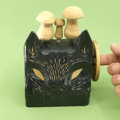 Gif of a wooden, block shaped black wolf head with small details carved exposing the natural wood. A handle on the right is being turned and is making the 3 wooden mushrooms atop its head move up and down.