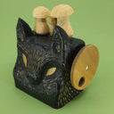 Side angle of a wooden, block shaped black wolf head with small details carved exposing the natural wood, there are 3 wooden mushrooms atop its head and a turnable disc handle on the side.