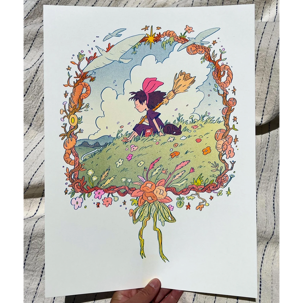 Risograph print of Kiki from Kiki's Delivery Service sitting on a green hilltop with a cloudy blue sky behind. She holds a broom and has a hand radio, with a black cat laying beside her. Scene is framed by a wreath made of bread, flowers and birds.