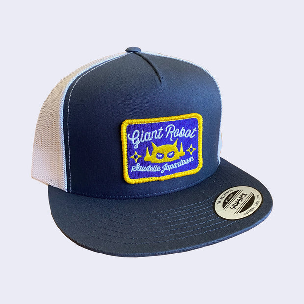Front of navy cap. Rectangle patch is outlined in yellow. Text around robot says sawtelle japantown. Back side of baseball cap is all white mesh.