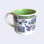 White ceramic mug with a metallic green interior and various illustrations on it, all within a color scheme of blue, pink, white and green. Illustrations include a bonsai tree, sashimi, sushi rolls, cherry blossoms, a food stall that says "Ketchie's Stand," a street sign that says "Sawtelle Japantown" and a shaved ice cone.