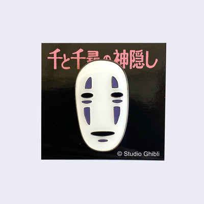 Enamel pin of a close up No Face head with a neutral expression on a black backing card with pink Japanese writing.