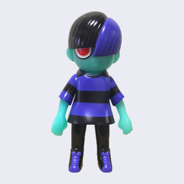 Vinyl figure of a green skin boy wearing a purple and black striped shirt, black pants and black sneakers with purple laces. He has one visible bright red eye that shows from behind duo tone black and purple bowl cut style hair.