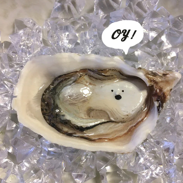 Sculpture of a small oyster in a half shell, with a surprised expression. A photoshopped speech bubble says "Oy!" It is in a bath of fake ice.