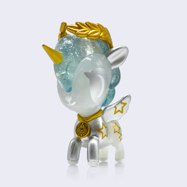 Vinyl unicorn figure, half silver and half semi translucent with gold necklace, horn, star pattern on its side and wings, and leaf crown on its head.