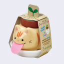 Small round ceramic orange cat planter with a large pink fabric tongue. It sits in a small round dish and is encased in cardboard packaging that reads "Peropon"