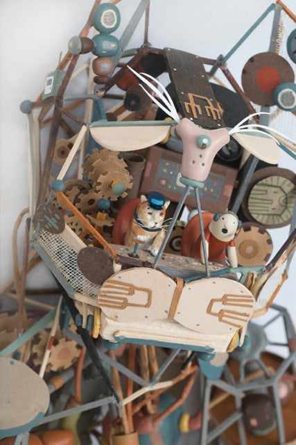 Photograph of a detailed diorama. A person and an orange tabby cat pilot an abstract flying devices, with lots of parts and pieces.