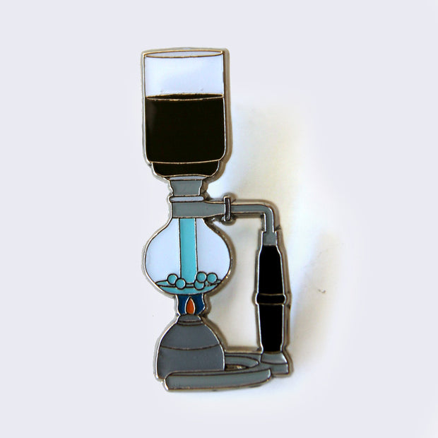 Enamel pin of a coffee siphon. Black coffee is on top, water is siphoning through a machine with gray and black accents.