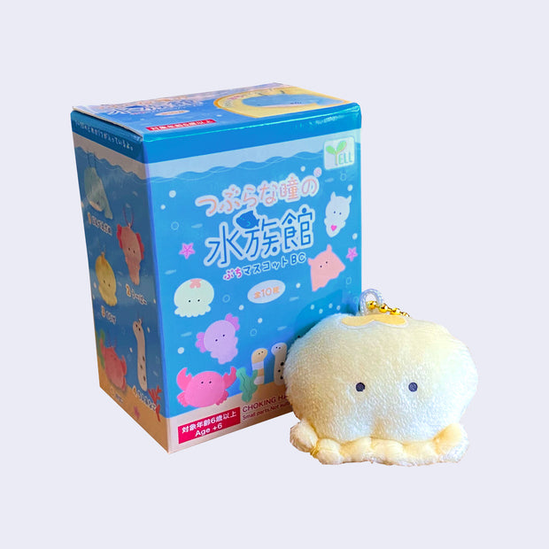 Small yellow plush octopus attached to a gold keychain, sitting in front of a blue product packaging.