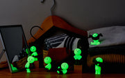 7 different glow in the dark Smiski figures, all getting dressed in various poses.