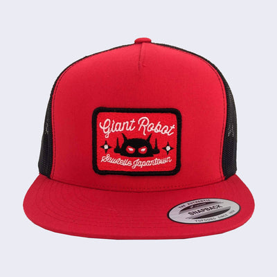 Front of red baseball cap. Rectangle patch is also red and is outlined in black. Cursive text around robot head says sawtelle japantown.