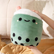 Rounded squishy sage green plush shaped like a boba tea cup, with a cute kawaii smile and a pink straw coming out of the top. Plush is being squished in someone's hands.