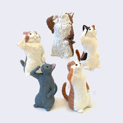 5 different small plastic cats, all standing propped up on their back paws and saltuting.