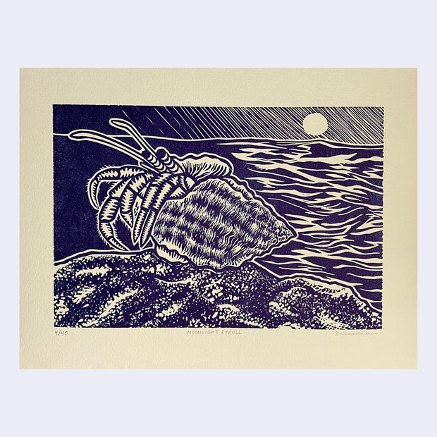 Linocut dark purple ink on cream paper of a hermit crab on a beach shore.