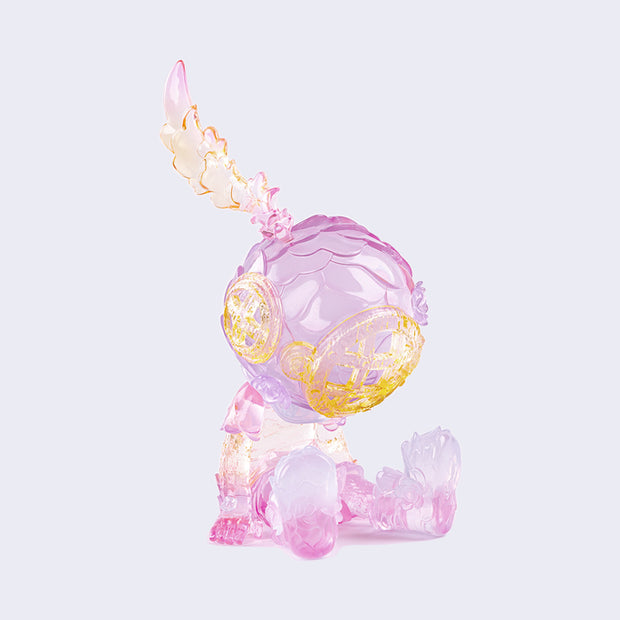 Semi transparent sculpted figure of a small person sitting with their hands at their side, legs out in front of them and wearing a scuba diving helmet with a feather coming out of the top. Figure is primarily light purple with yellow ombre elements.