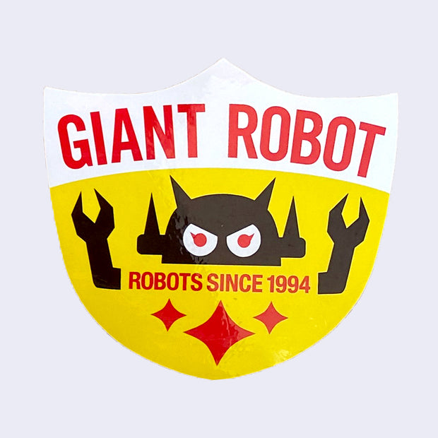 Yellow shield shaped sticker, with white top. "Giant Robot" is written in red bold font along top. A Big Boss Robot head is above "Robots Since 1994" with arms coming out of the text. 3 red sparkles are on the bottom.