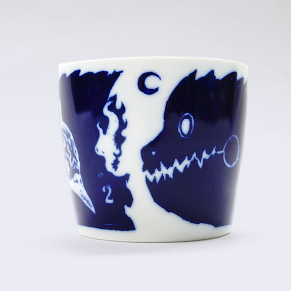 White ceramic cup with a wrap around dark blue illustration. Current side features a silhouette of a monster's head with jagged teeth and a small moon in the upper center. 