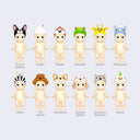 12 vinyl Kewpie babies, standing nude with different animals atop their heads like hood hats. Options are: french bulldog, snake, macaw, crocodile, giraffe, rhino, zebra, toy poodle, chihuahua, lop ear rabbit, shorthair cat, and parrot.