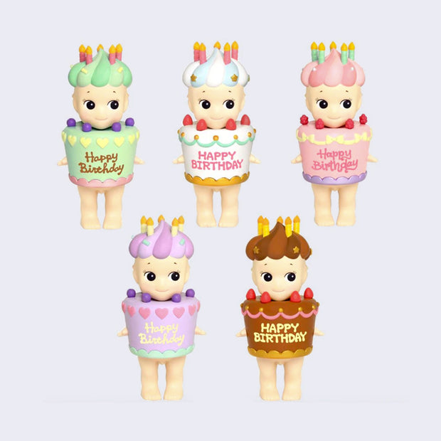 5 different Sonny Angels wearing a large decorated cake as an outfit with strawberries. It says "Happy Birthday" on it. Atop the Sonny Angel's head is a swirled hat of matching colored frosting with candles on top. Color ways include: green, white with blue, pink, purple and brown.