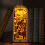 3D puzzle kit to build a bookend, with scenery of an alleyway containing bookshops and other shopping center visuals. Glowing from an interior light and between several books.