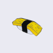 Enamel pin of tamago nigiri. The yellow egg sits atop white rice and both are wrapped with a strip of black seaweed.