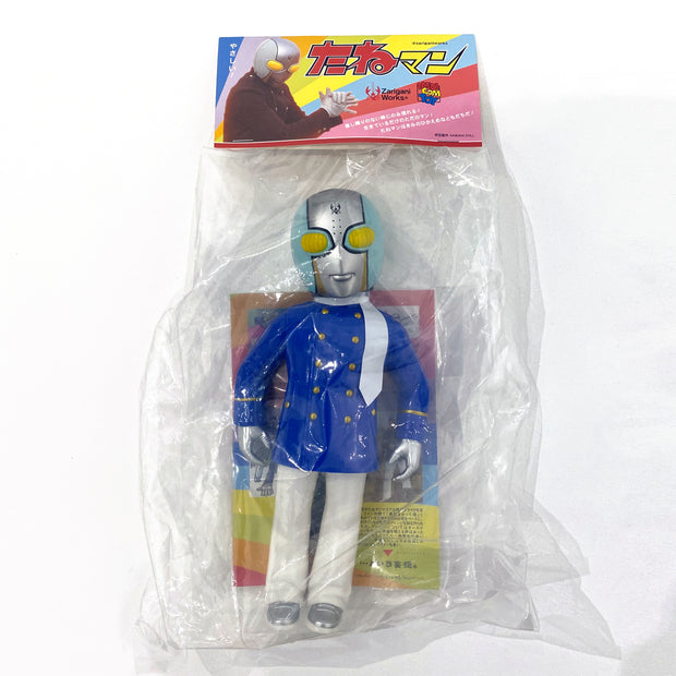 Bagged plastic figure of a person wearing a blue coat with gold buttons, white pants and a white fashion scarf. It wears a helmet reminiscent of a Japanese sentai character, silver with blue accents and yellow eyes. 