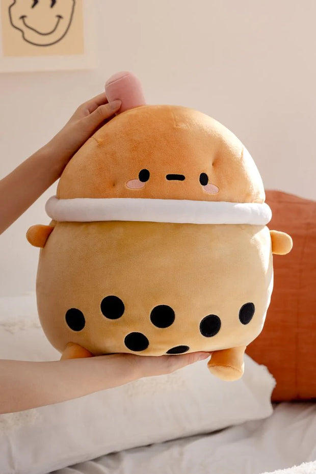 A squishy plush shaped like a potato character, dressed up as a cup of boba tea with a pink straw. Plush is being held up in someone's hands.