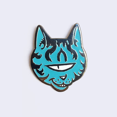 Enamel pin of blue, one-eyed cat head with sneaky expression and smile. Cat has metallic stripes on head and cheeks.