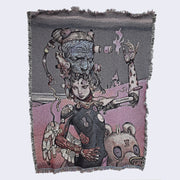 Spread out tapestry blanket, half gray and half dusty rose with intentionally frayed edges. Tapestry design features a topless half mechanical woman, looking off to the side. Atop her head is a large head of an elderly man, with smoke coming out of a helmet pipe. Part of a pig-like robot emerges near her torso. 