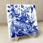 White ceramic square tile with a deep blue line illustration of a woman with a face tattoo, wearing a helmet and looking off to the side, an empty speech bubble coming out of her. A crocodile with a headband rests its head on her shoulder. Tile is displayed on a clear acrylic stand.